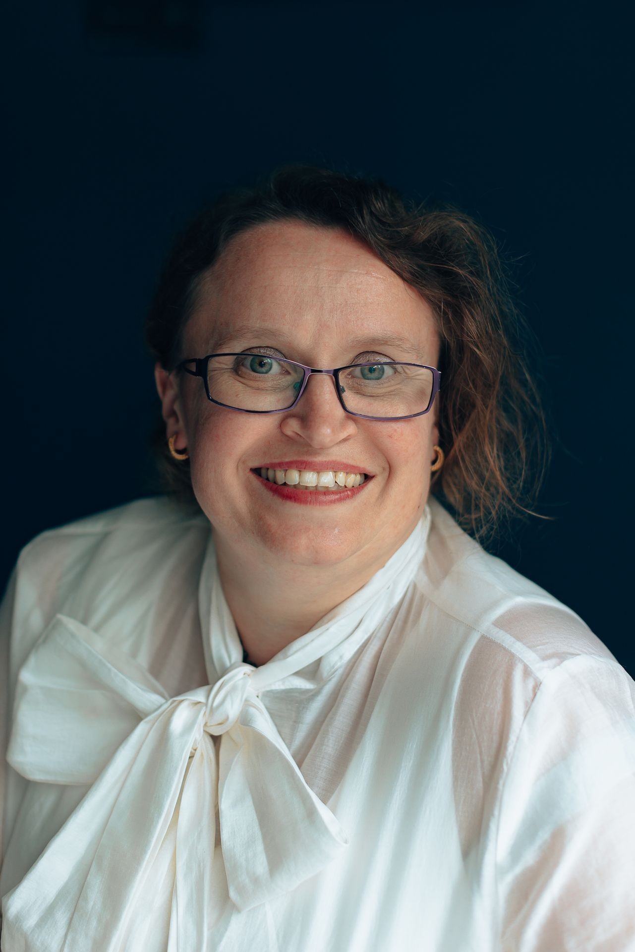 Person wearing a white blouse with a large bow, set against a dark background.